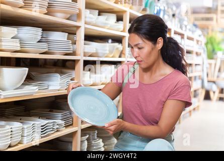 Positive weibliche Käufer wählt neue Teller im Geschirrladen Stockfoto