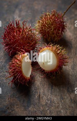 Nahaufnahme von reifem Rambutan, geschälten und ganzen saftigen tropischen Früchten aus südostasien, verstreut auf hölzernen Tischplatten, sanfter Fokus mit Kopierraum Stockfoto