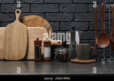 Schneidebretter aus Holz, Utensilien, Mokakanne und Tasse auf grauem Tisch in der Nähe einer dunklen Ziegelwand Stockfoto