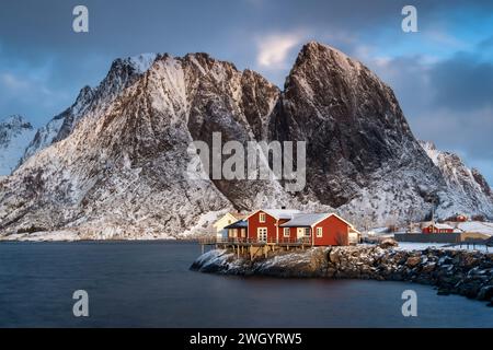 Rotes norwegisches Rorbuer-Haus und Festhaeltinden-Berg im Winter, reine, Moskenes Municipality, Nordland County, Lofoten Islands, Norwegen Stockfoto