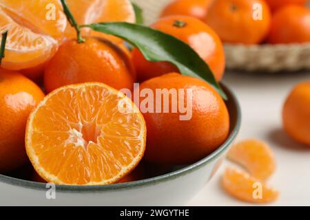 Köstliche Mandarinen mit grünen Blättern in Schüssel auf weißem Holztisch, Nahaufnahme Stockfoto