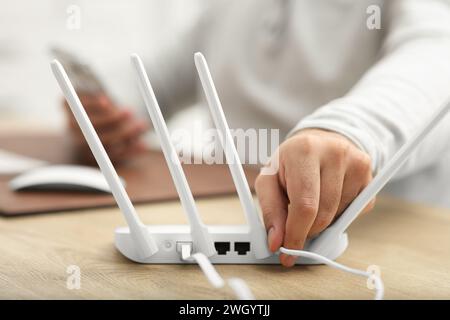 Mann, der Kabel in den WLAN-Router an einem Holztisch drinnen steckt, Nahaufnahme Stockfoto