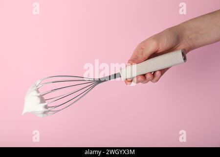 Frau mit Schneebesen mit Schlagsahne auf rosa Hintergrund, Nahaufnahme Stockfoto