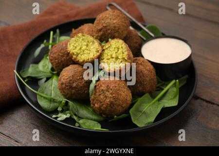 Köstliche Falafelbällchen, Kräuter und Soße auf Holztisch Stockfoto