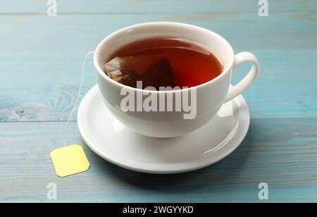 Teebeutel in der Tasse mit heißem Getränk auf hellblauem Holztisch, Nahaufnahme Stockfoto