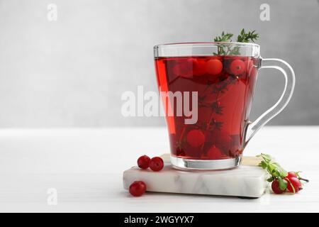 Leckerer heißer Preiselbeertee mit Thymian und frischen Beeren in Glasbecher auf weißem Holztisch Stockfoto