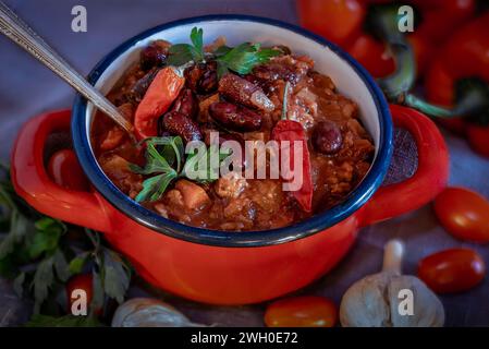 Scharfe Chili con Carne mit Kidneybohnen und Paprika im roten Keramiktopf Stockfoto