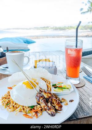 Mie Goreng (gebratene Nudeln) serviert mit zwei Hähnchensatay und einem Spiegelei in einem Restaurant am Medewi Beach in Bali, Indonesien. Stockfoto