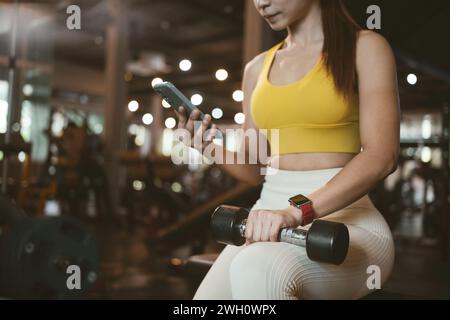 Junge Frau, die ein Telefon im Fitnessstudio benutzt. Stockfoto