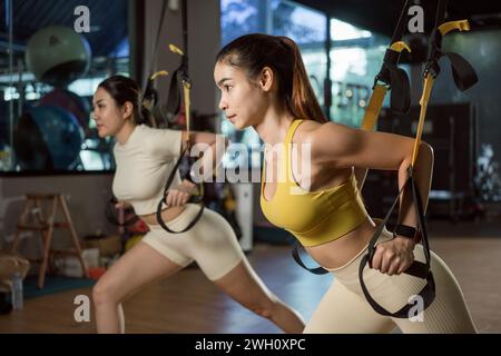 Asiatische Frau macht Liegestütze, Armtraining mit trx Fitnessgurten im Fitnessstudio. Stockfoto