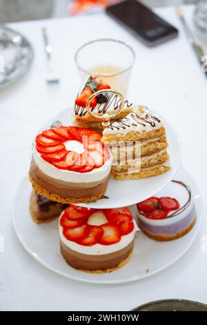 Eine elegante Präsentation von Kuchen und Gebäck auf einem dreistufigen Stand mit einem Glas Orangensaft. Das Bild strahlt Luxus und Raffinesse aus, perfekt Stockfoto