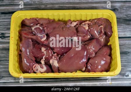 Rohe Hühnerlebern, Magen und Herzen, frische Leber, Magen und Herz von Hühnern voller Eiweiß auf einer gelben Einwegplatte isoliert auf Holzbaa Stockfoto