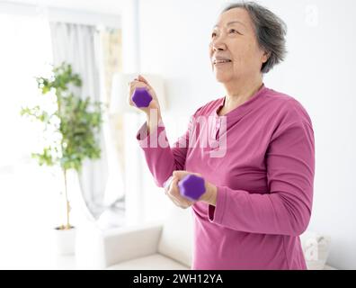 Asiatische Seniorin macht Übungen mit Kurzhanteln drinnen. Stockfoto