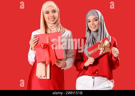 Junge muslimische Frauen im Hijab mit Geschenken auf rotem Hintergrund Stockfoto