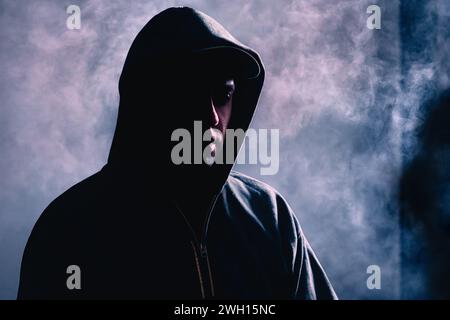 Krimineller Mann im Schatten. Unheimlicher verdächtiger Fremder mit verstecktem Gesicht. Silhouette eines Gangsters mit dunklem Rauchnebel Hintergrund. Bandenkriminalität oder Horror. Stockfoto