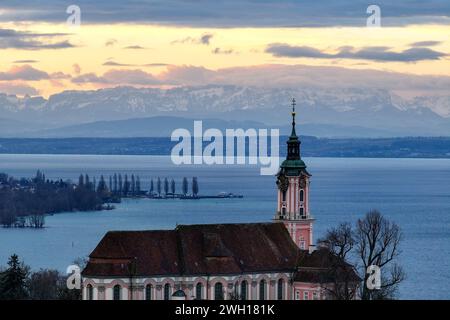 Unteruhldingen Am Bodensee, Deutschland. Februar 2024. Die Sonne geht hinter der ehemaligen Klosterkirche Birnau am Bodensee auf. Die Alpen sind im Hintergrund zu sehen. Windig, regnerisch, aber mild: Das Wetter wird in den nächsten Tagen ziemlich unangenehm sein. Der Deutsche Wetterdienst hat bis Freitag Dauerregen für Mitteldeutschland prognostiziert. In den östlichen Mittelgebirgen kann der Niederschlag auch gelegentlich zu Schnee werden. Aufgenommen mit einer Drohne Credit: Felix Kästle/dpa/Alamy Live News Stockfoto