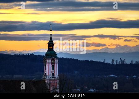 Unteruhldingen Am Bodensee, Deutschland. Februar 2024. Die Sonne geht hinter der ehemaligen Klosterkirche Birnau am Bodensee auf. Die Alpen sind im Hintergrund zu sehen. Windig, regnerisch, aber mild: Das Wetter wird in den nächsten Tagen ziemlich unangenehm sein. Der Deutsche Wetterdienst hat bis Freitag Dauerregen für Mitteldeutschland prognostiziert. In den östlichen Mittelgebirgen kann der Niederschlag manchmal auch in Schnee übergehen (Drohnenschuss) Credit: Felix Kästle/dpa/Alamy Live News Stockfoto