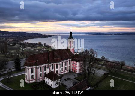 Unteruhldingen Am Bodensee, Deutschland. Februar 2024. Die Sonne geht hinter der ehemaligen Klosterkirche Birnau am Bodensee auf. Die Alpen sind im Hintergrund zu sehen. Windig, regnerisch, aber mild: Das Wetter wird in den nächsten Tagen ziemlich unangenehm sein. Der Deutsche Wetterdienst hat bis Freitag Dauerregen für Mitteldeutschland prognostiziert. In den östlichen Mittelgebirgen kann der Niederschlag auch gelegentlich zu Schnee werden. Aufgenommen mit einer Drohne Credit: Felix Kästle/dpa/Alamy Live News Stockfoto