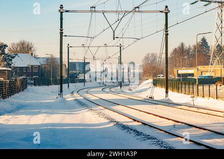 Stromkabel auf schneebedeckten Bahngleisen zwischen Häusern und Gebäuden, verschwommener nebeliger Hintergrund, sonniger Tag nach starkem Schneefall in Beek-Elsloo, Stockfoto