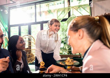 Lächelnde Kellnerin serviert im Restaurant Mahlzeiten für eine Gruppe von Geschäftsleuten. Stockfoto