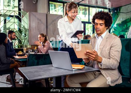 Lächelnde Kellnerin, die Befehle eines afroamerikanischen Geschäftsmannes im Restaurant entgegennimmt. Stockfoto