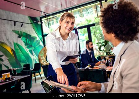 Lächelnde Kellnerin, die Befehle eines afroamerikanischen Geschäftsmannes im Restaurant entgegennimmt. Stockfoto