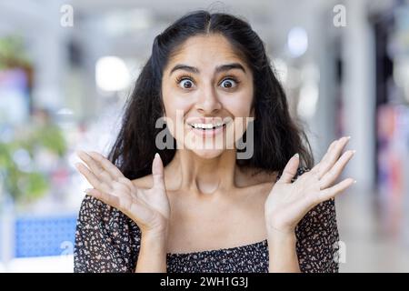 Eine überschwängliche Indianerin in einem Einkaufszentrum, ihre Hände drücken Freude mit mehreren bunten Einkaufstaschen aus. Stockfoto
