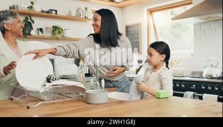 Das Kind putzt die Küche mit ihrer Großmutter und Mutter, während es sich verbindet, redet und lacht. Happy, Lächeln und Mädchen, die das Geschirr mit ihr waschen Stockfoto