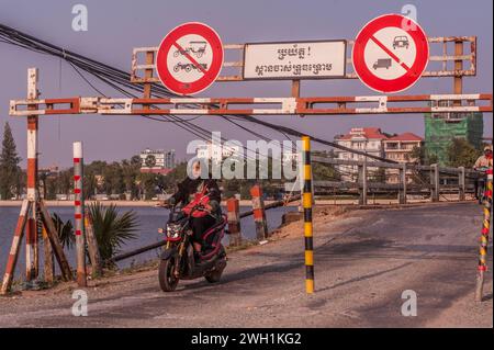 Eine Cham oder Muslimin fährt mit ihrem Motorrad durch den Eingang zur alten Französischen Brücke auf dem Praek Tuek Chhu Fluss. Kampot, Kambodscha. © Kraig Lieb Stockfoto