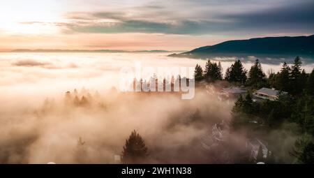 Ein Blick aus der Vogelperspektive auf den nebeligen Sonnenuntergang über den grünen Bergen Stockfoto