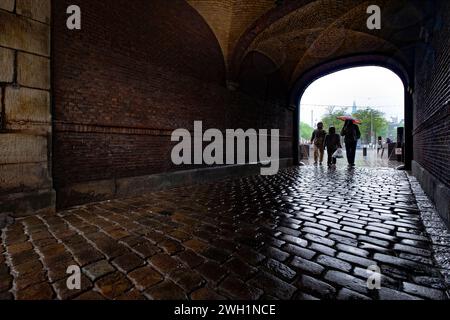 Die Menschen schützen vor dem Regen mit Regenschirmen in einem Steinbogen im Binnenhof in der Stadt Haag, Niederlande Stockfoto