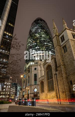 London. UK-02.02.2024. Nächtlicher Blick auf das Gherkin-Gebäude in der City of London mit St. Andrew Undershaft Kirche vorne. Stockfoto