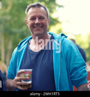 Porträt, Bier und Mann bei Outdoor-Party, Feier oder fröhlichem Abenteuer bei Feiertagen in Deutschland. Lächeln, Getränke und Natur, reifer Mensch Stockfoto