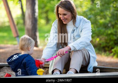 Die Mutter mit ihrem Kind macht Spaß auf dem Spielplatz. Kleiner Junge mit ihrer Mutter, die in der Sandbox spielt Stockfoto