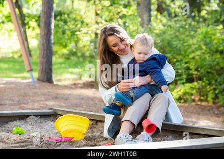 Die Mutter mit zwei Kindern macht Spaß auf dem Spielplatz. Zwei kleine Jungs mit ihrer Mutter, die in der Sandbox spielt Stockfoto