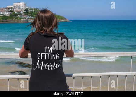 Eine Frau, die ein T-Shirt mit I'm Get Married trägt, bedruckt auf der Rückseite, um Towan Beach in Newquay in Cornwall in Großbritannien zu sehen. Stockfoto