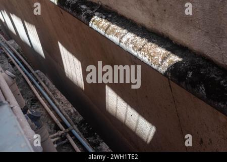 Sonnenlicht, das durch ein Hindernis durchdringt, erzeugt ein deutliches Muster von Schatten auf einer strukturierten Wand, das auf einen sonnigen Tag hinweist. Stockfoto