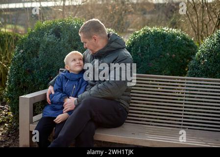 Herbstliche Familienzusammenhänge: Vater, 40 Jahre alt, und Sohn - wunderschöner 8-jähriger Junge, im Park sitzend. Stockfoto
