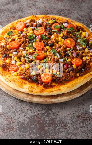 Hausgemachte, scharfe mexikanische Taco-Pizza mit Hackfleisch, Tomaten, Mais, schwarzen Bohnen, Cheddar-Käse, rote Zwiebel auf dem Holzbrett auf dem Tisch. Vertikal Stockfoto