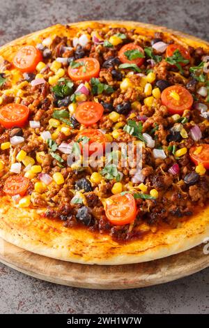 Tex Mex Taco-Pizza mit Hackfleisch, Tomaten, Mais, schwarzen Bohnen, Cheddar-Käse, rote Zwiebeln und mexikanische Gewürze aus nächster Nähe auf einem Holzbrett auf dem Tisch Stockfoto
