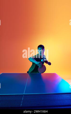 Asiatischer Mann, Tischtennisspieler, der im Neonlicht vor warmgelbem Hintergrund schlägt. Dynamisches Gelporträt. Stockfoto