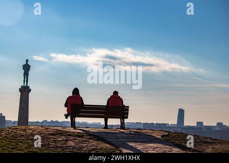 Zwei Freunde draußen an einem schönen sonnigen Tag, sitzen auf der Bank der Kalemegdan-Festung in Belgrad, mit wunderschönem Blick auf die Siegesstatue (Pobednik) Stockfoto