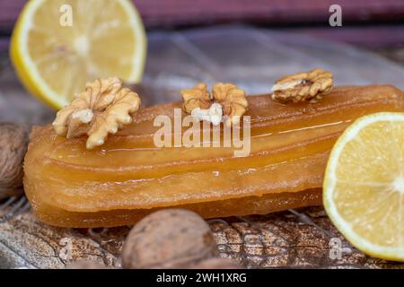 Türkischer süßer Kuchen namens Tulumba, serviert auf einem Teller mit Zitronenscheiben und Nüssen, auf einem massiven Holztisch Stockfoto