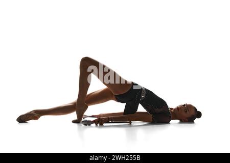 Flexibles, talentiertes Teenager-Mädchen, akrobat in schwarzem Bodysuit, rhythmische Turnerin, die vor weißem Studio-Hintergrund auftritt Stockfoto