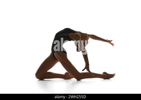 Flexibles, talentiertes Teenager-Mädchen, akrobat in schwarzem Bodysuit, rhythmische Turnerin, die vor weißem Studio-Hintergrund auftritt Stockfoto