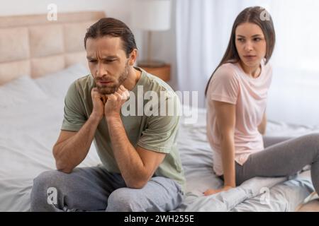 Mann, der im Bett nachdenkt, Frau, die dahinter sitzt Stockfoto