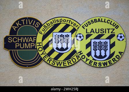 Hoyerswerda, Deutschland. Februar 2024. Die Logos der Vereine „Aktivist Schwarze Pumpe“, „Fußballsportverein Hoyerswerda“ und „Fußballclub Lausitz Hoyerswerda“ sind auf dem Funktionsgebäude neben dem Friedrich-Ludwig-Jahn-Stadion im Stadtteil Bautzen montiert. Robert Michael/dpa/Alamy Live News Stockfoto