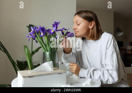 Saisonale Allergikerfrei. Junge Frau schnüffelt von Irisblumen, genießt den Geruch ohne laufende Nase, Jucken oder Husten saisonale Symptome in gemütlichem Zuhause. Gir Stockfoto