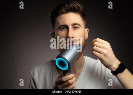Porträt eines langbärtigen Mannes mit Haarfön und Kamm zu Hause, dunkler Hintergrund, Nahaufnahme Stockfoto