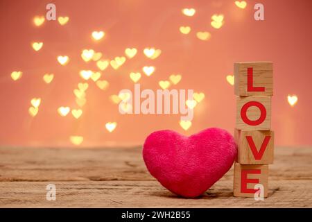 Holzwürfel mit rotem Text Love und kleinem rosa flauschigem Herz Platz neben auf Holztisch mit Kopierraum, defokussiertes herzförmiges Bokeh-Licht Stockfoto